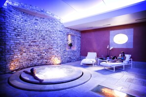 Een wellnessruimte met een stenen muur, een jacuzzi en twee ligstoelen.
