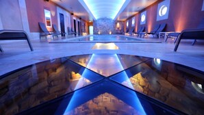 Un spa moderno con una piscina reflectante central, sillones de descanso y una pared de piedra al fondo.