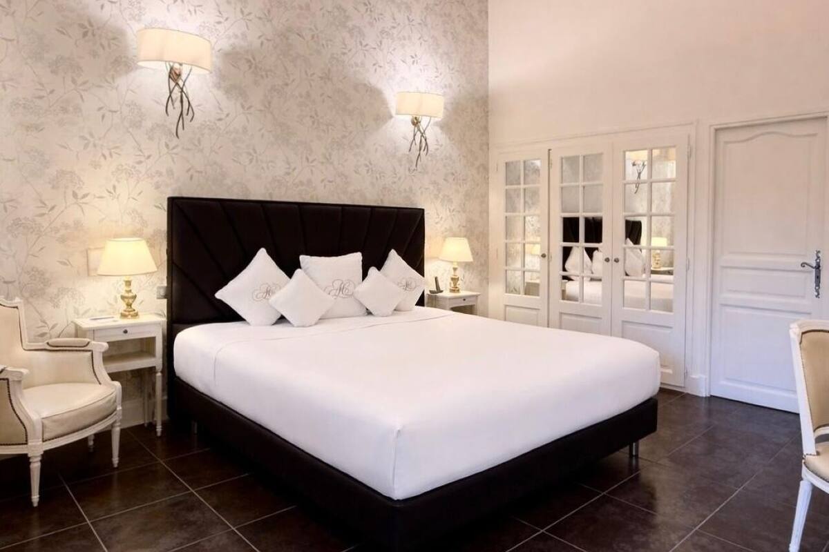 Une chambre à coucher avec un grand lit, deux tables de chevet avec des lampes, une chaise et une armoire aux portes en verre.