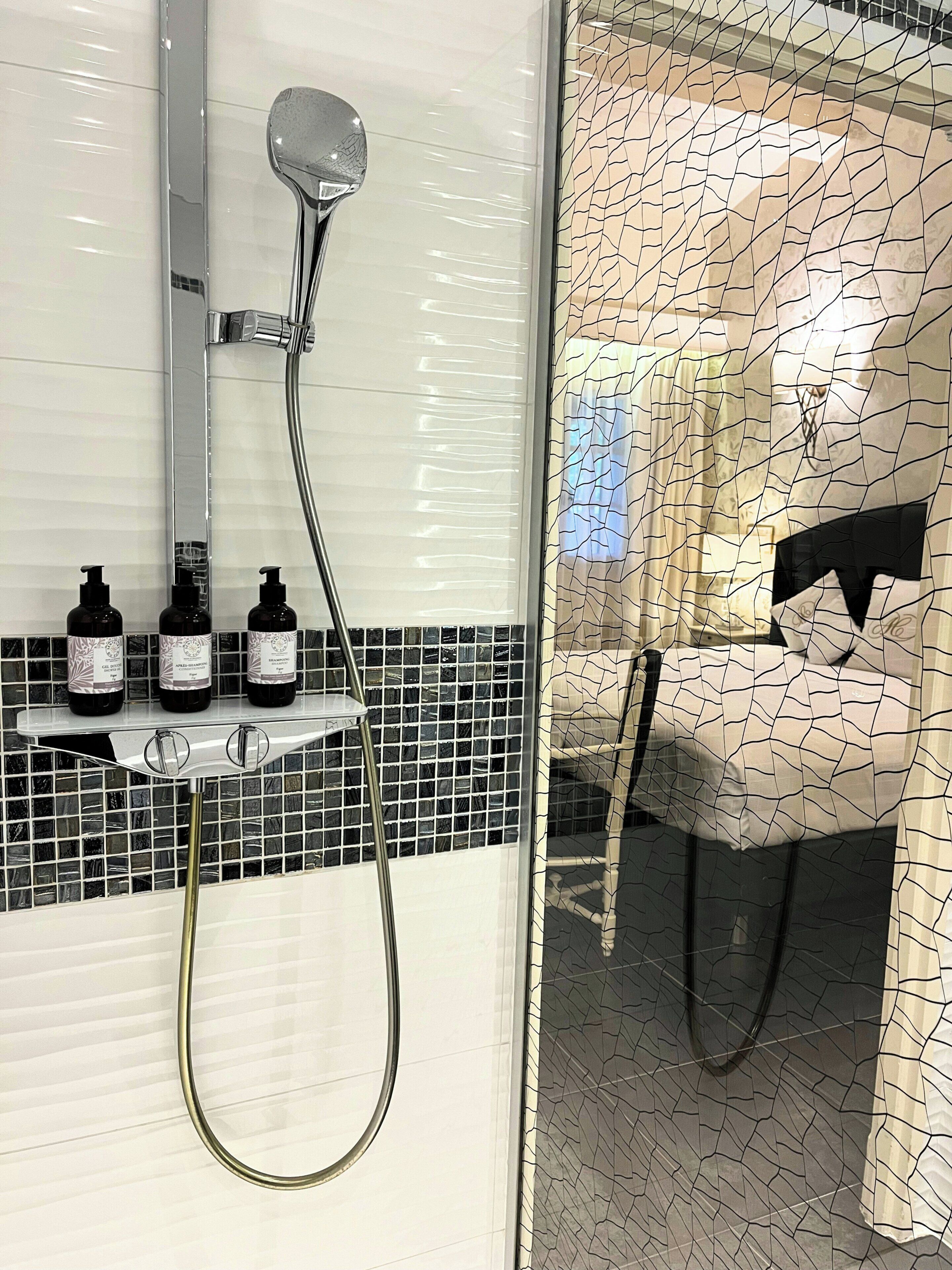 Un baño con ducha, lavamanos y tres botellas de champú en un estante.