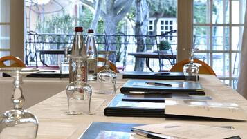 Une table de conférence, sur laquelle sont disposés des documents, des stylos et des verres, se trouve dans une pièce dotée de grandes fenêtres offrant une vue sur les arbres et les bâtiments environnants.
