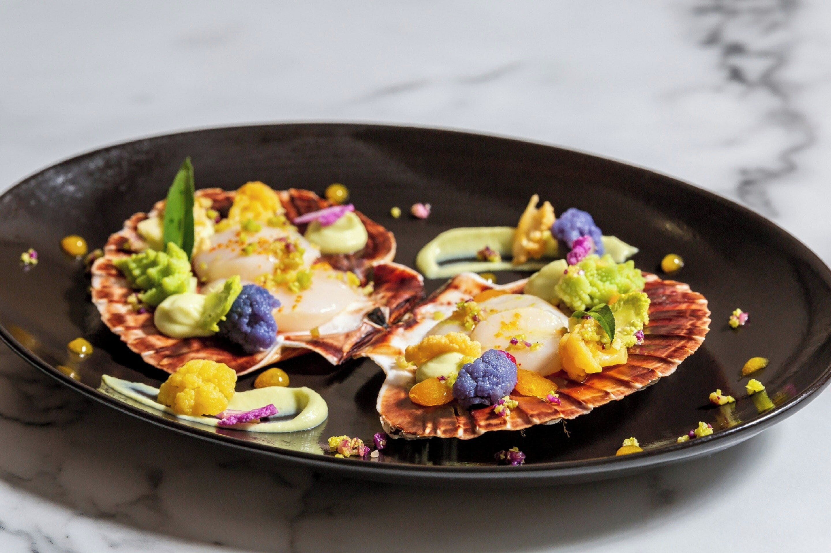 A plate with scallops, avocado, and colorful garnishes.