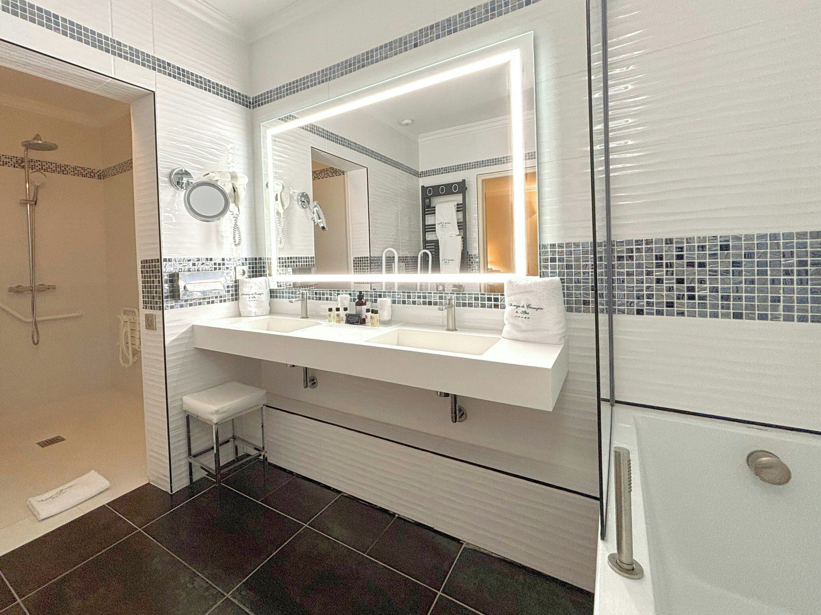 A modern bathroom with a double sink, a large mirror, a shower, and a toilet.