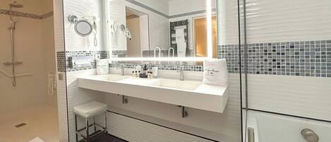 A modern bathroom with a double sink, a large mirror, a shower, and a toilet.