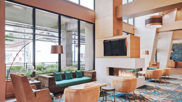 A modern lounge area with a sofa, armchairs, a fireplace, and a large window offering a view of the city. - Residence Inn by Marriott Vancouver Downtown (Vancouver)