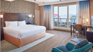 A hotel room with a large bed, a desk with a chair, a small table, and a balcony with a view of buildings. - Residence Inn by Marriott Vancouver Downtown (Vancouver)