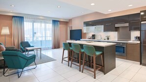 A modern kitchen with a central island, bar stools, a dining area with a table and chairs, and a large window with curtains. - Residence Inn by Marriott Vancouver Downtown (Vancouver)