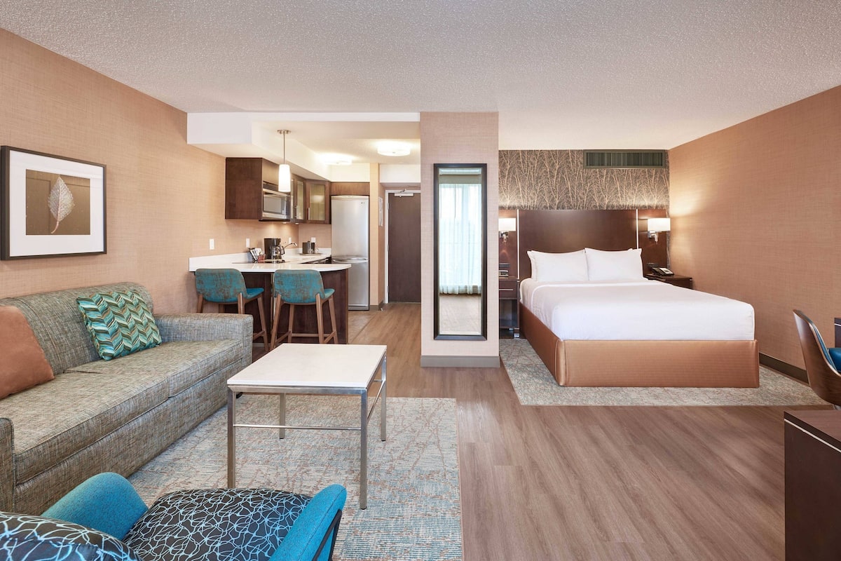 A hotel room with a bed, a sofa, a dining area, and a kitchenette.