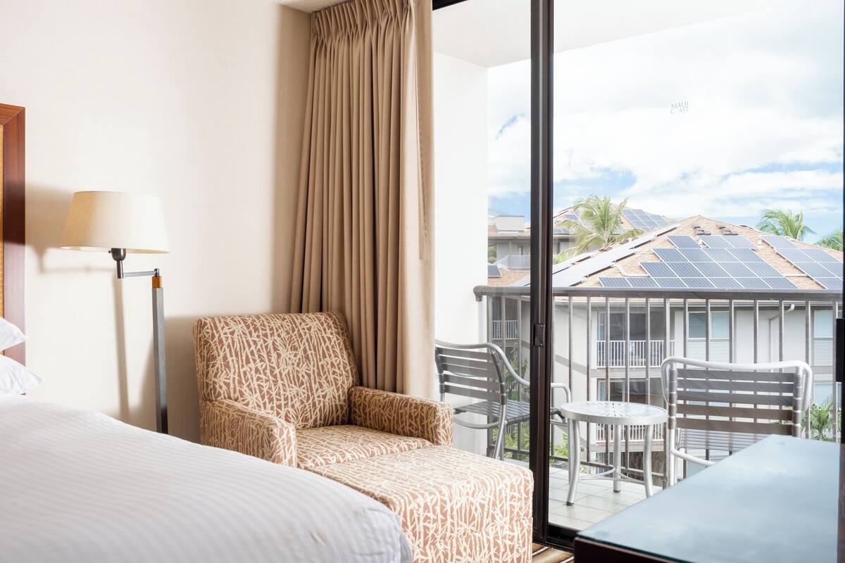 Una habitación de hotel con una cama, un sillón estampado, una mesa y vistas a paneles solares en el techo.
