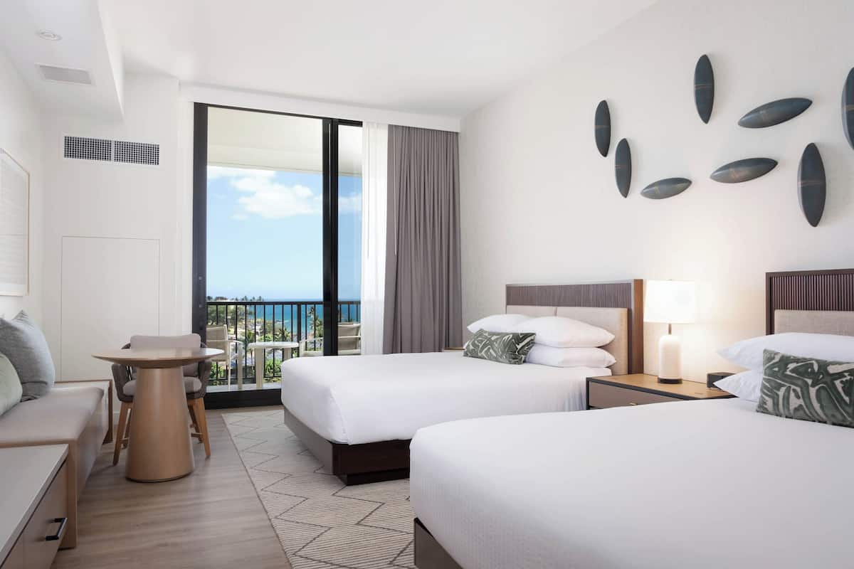 Habitación de hotel con dos camas, una mesita, un sofá y un balcón con vistas.