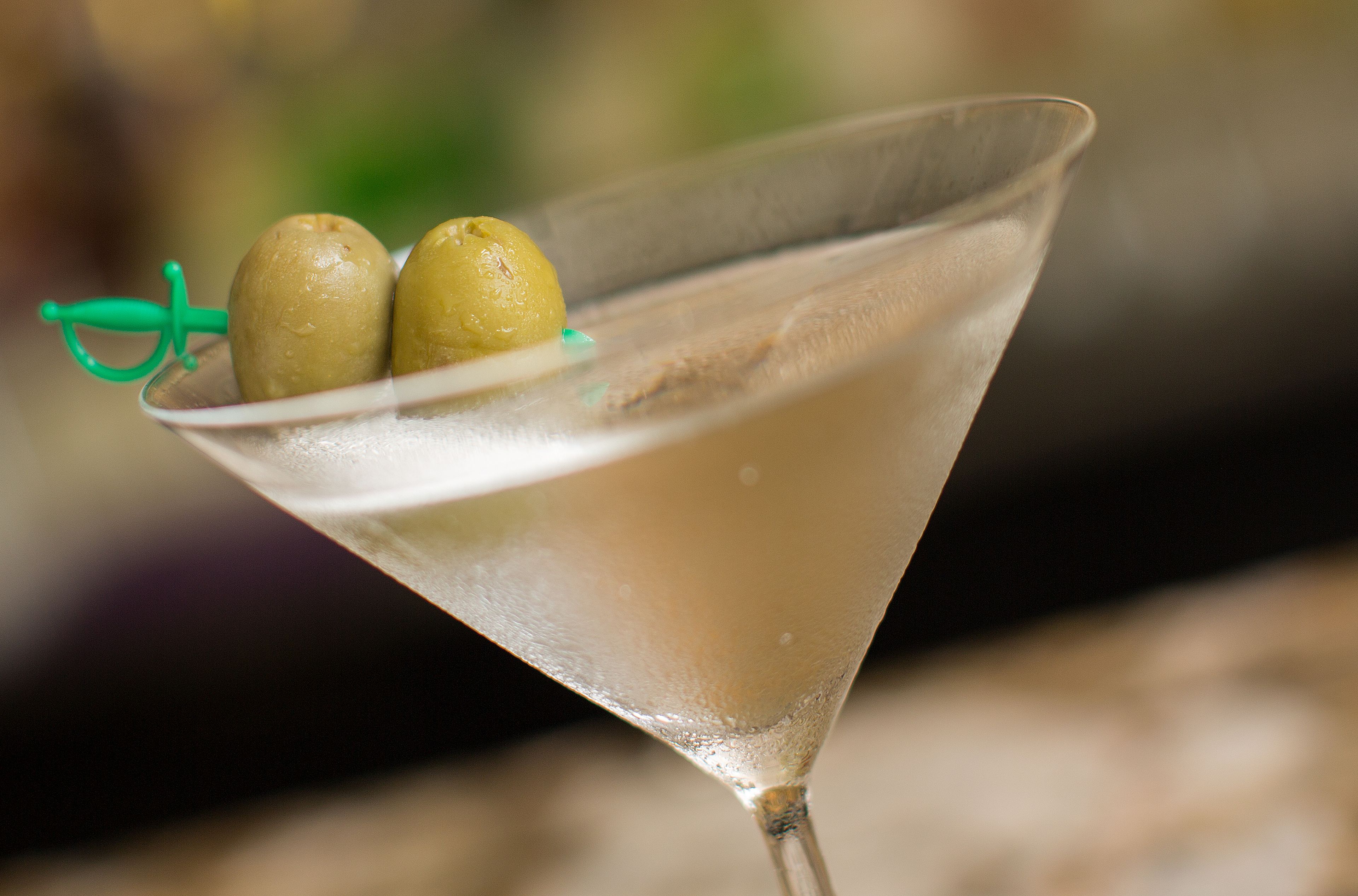 A martini glass with two olives on a green olive pick.