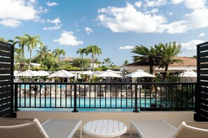 A poolside area with lounge chairs and umbrellas, a clear blue sky, and palm trees.