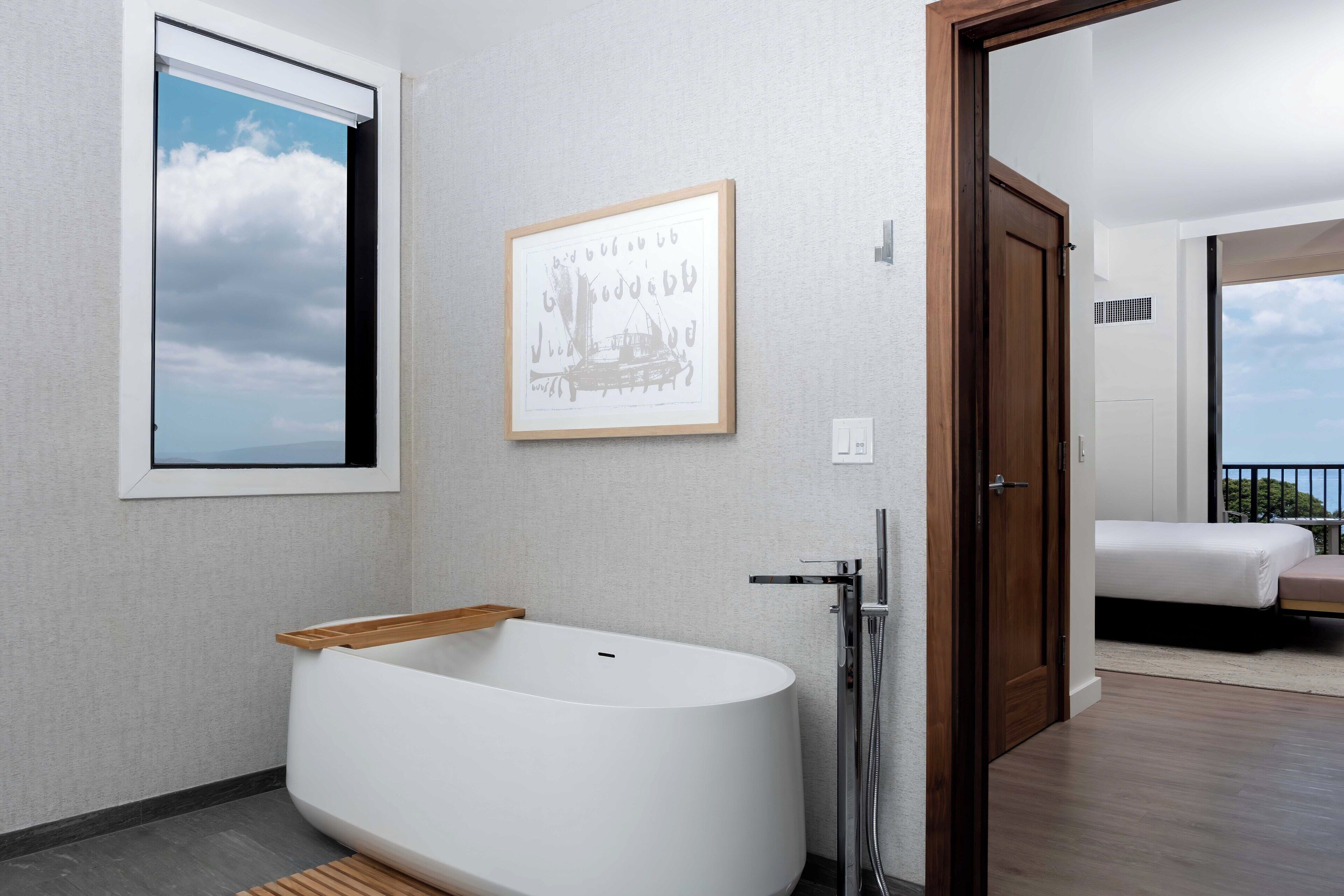 Un bagno moderno con una vasca freestanding, un quadro appeso alla parete e una porta che dà su un balcone con un letto.
