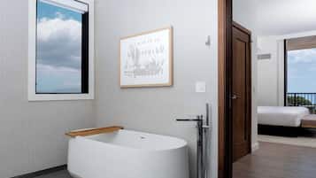 Un bagno moderno con una vasca freestanding, un quadro appeso alla parete e una porta che dà su un balcone con un letto.