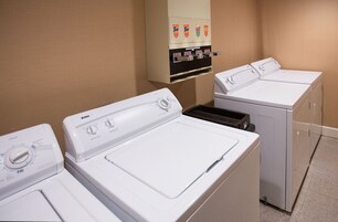 A laundry area with multiple washers and dryers, a control panel with detergent dispensers, and a wall-mounted cabinet.