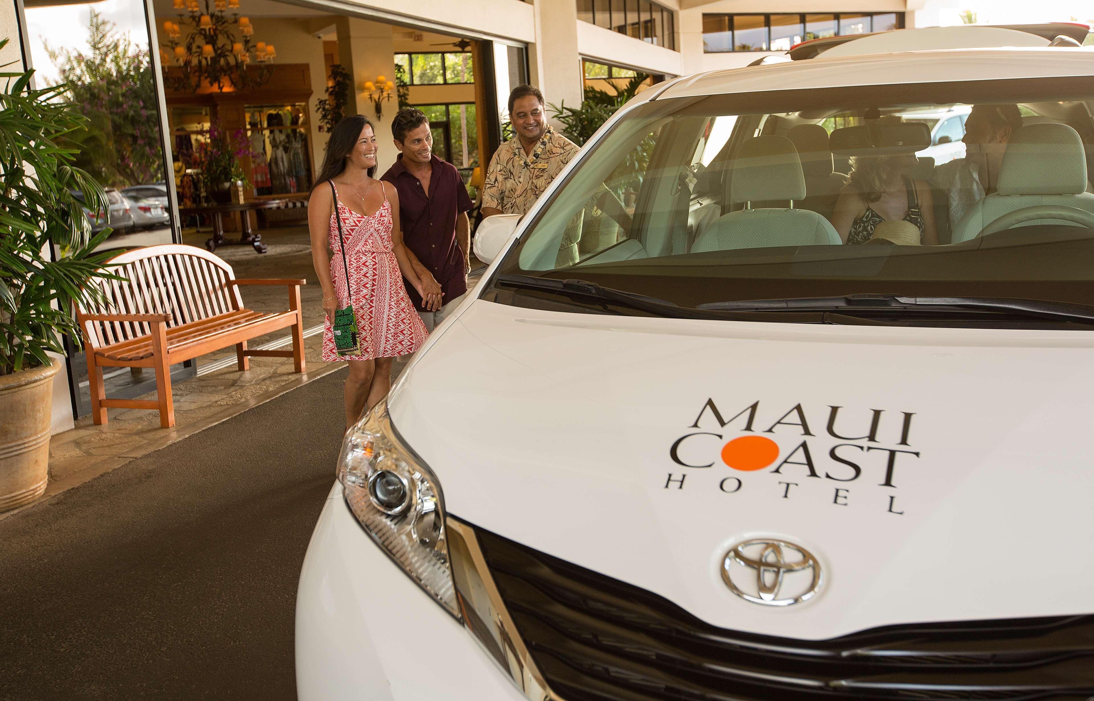 En hvid bil med 'Maui Coast Hotel' står parkeret foran en bygning.