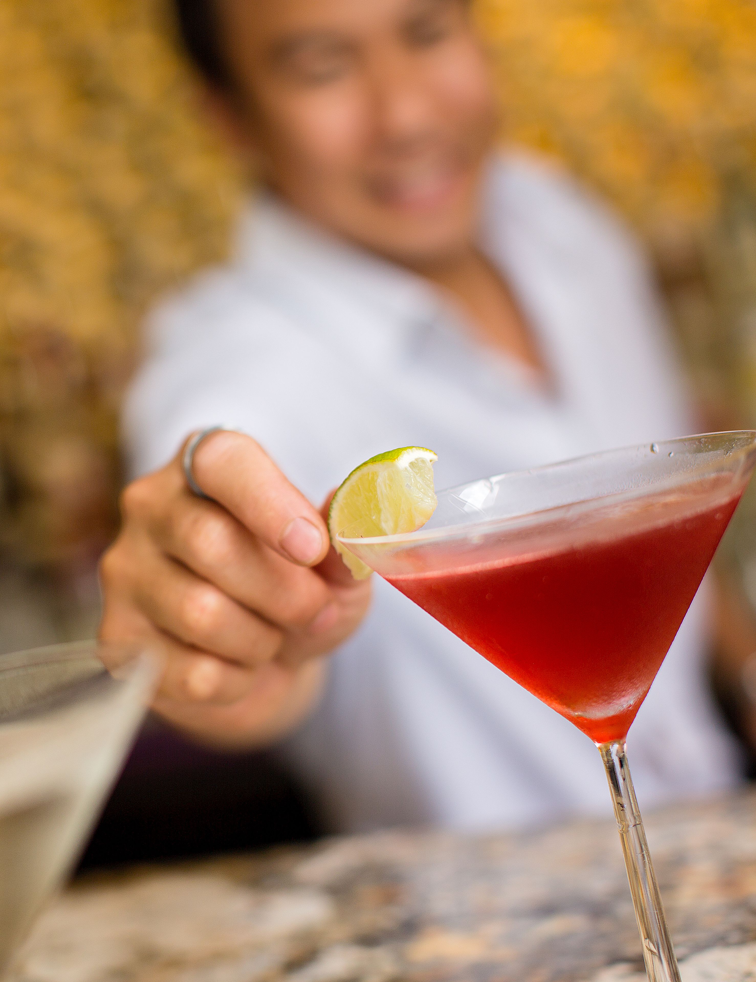 A close-up of a cocktail with a lime garnish, held by a person.