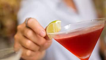 A close-up of a cocktail with a lime garnish, held by a person.