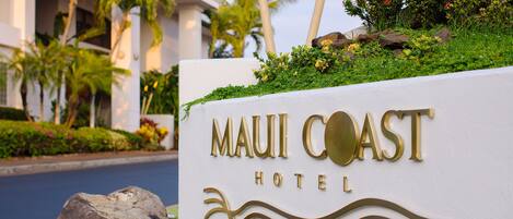 A sign for the Maui Coast Hotel with a wave design and palm trees in the background.