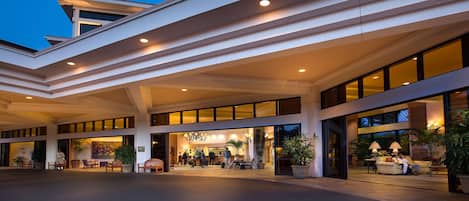 Una entrada de hotel moderna con un vestíbulo amplio, ventanas grandes y una zona de recepción bien iluminada.