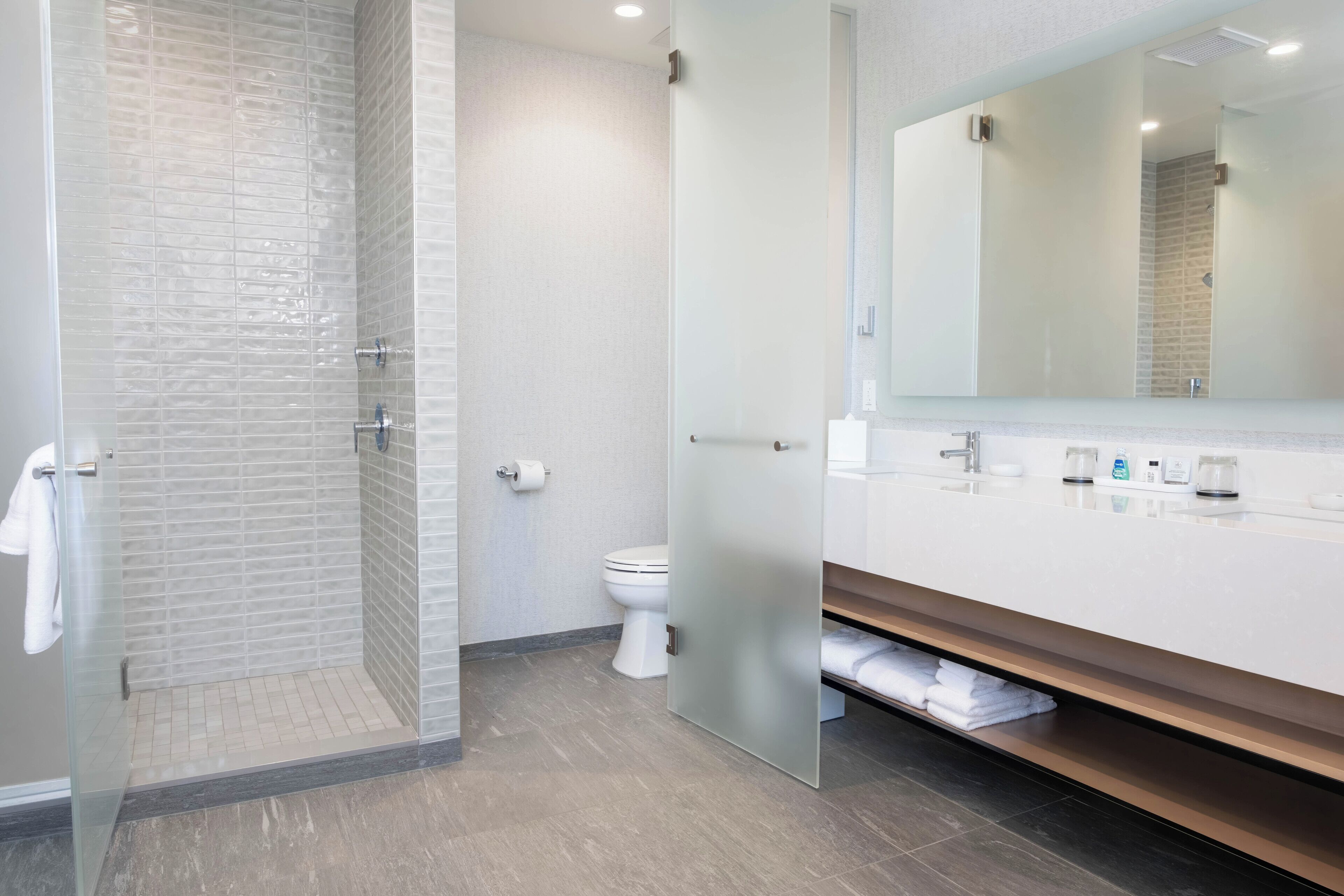 A modern bathroom with a glass shower enclosure, a white toilet, and a large mirror above a white vanity.