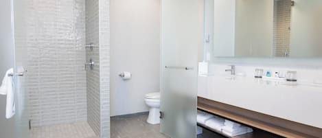 A modern bathroom with a glass shower enclosure, a white toilet, and a large mirror above a white vanity.