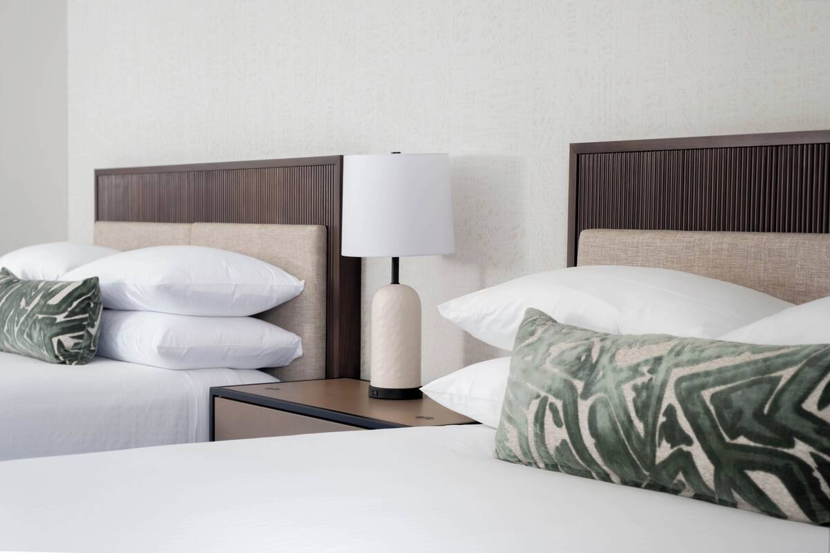 Una cama bien hecha con almohadillas blancas y verdes estampadas, una mesita de noche con una lámpara y un cabecero con líneas verticales.