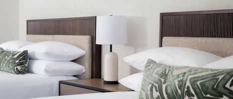 A neatly made bed with white and green patterned pillows, a bedside table with a lamp, and a headboard with vertical lines.