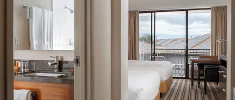 A hotel room with a bathroom, a bed, a desk, and a view of solar panels.