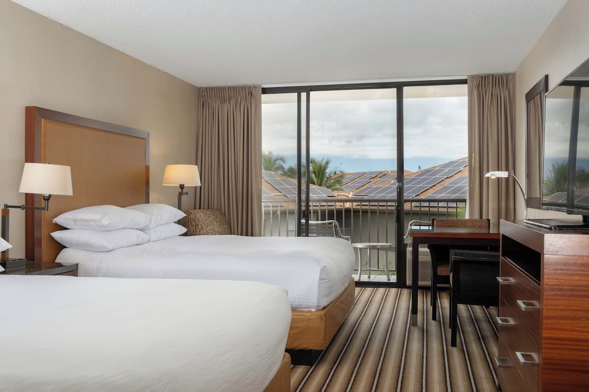 Habitación de hotel con dos camas, un escritorio, una silla y vistas a paneles solares.