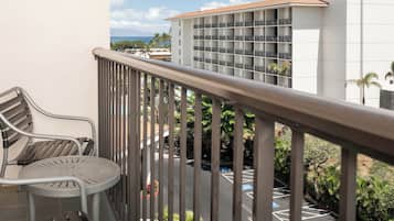 A balcony with a metal railing, a metal chair, and a small table. In the background, there is a building with multiple floors and a parking area with blue parking space markings.