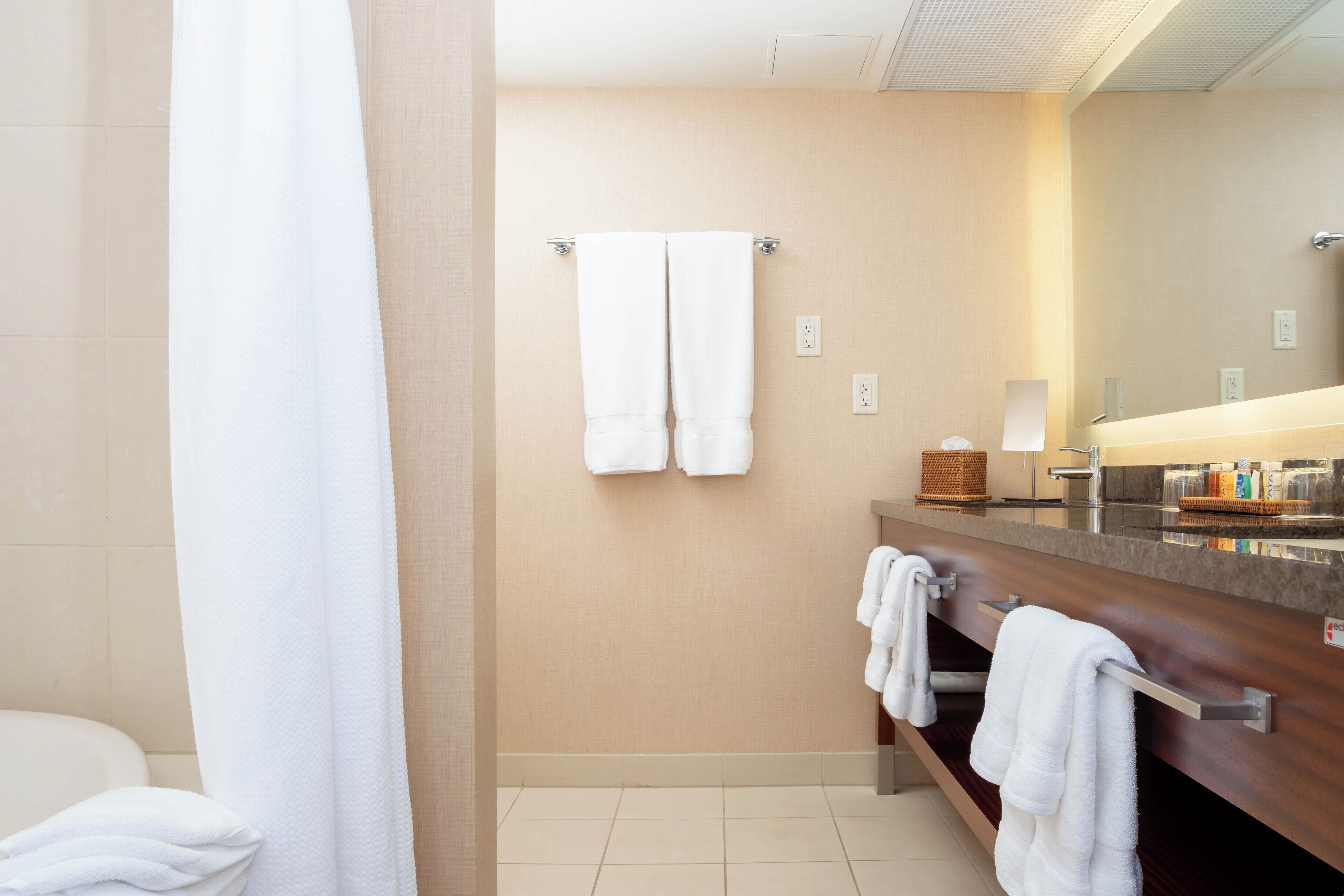 Un bagno moderno con una parete color crema, un mobile bagno in legno, un ampio specchio e due asciugamani appesi a un portascopevoli.