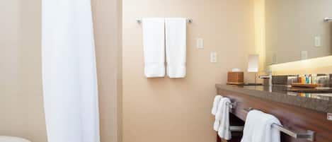 A modern bathroom with a beige wall, a wooden vanity, a large mirror, and two towels hanging on a towel rack.