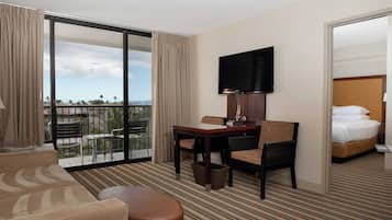 A hotel room with a balcony, a bed, a desk with a chair, and a television.