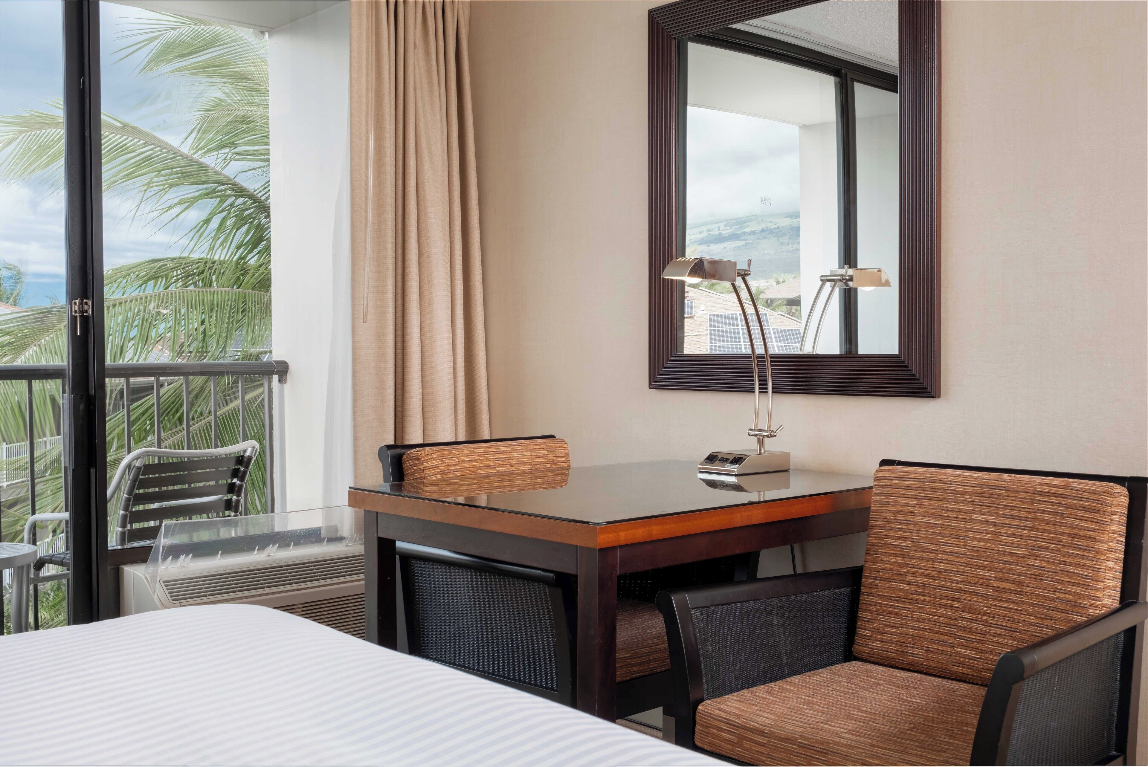 Een hotelkamer met balkon, een bed, een bureau met stoel en een grote spiegel.