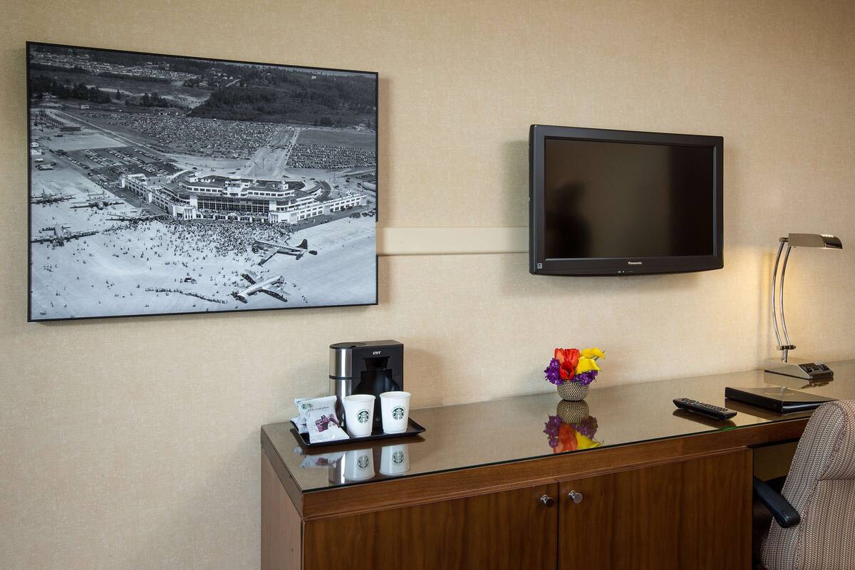 A hotel room with a mounted television, a coffee machine, and a Starbucks cup holder.