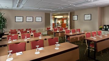 Ett konferensrum med bord och stolar, inramade tavlor på väggarna och en växt i hörnet.