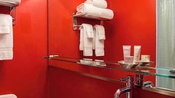 A bathroom with a red wall, a glass shelf with toiletries, and a mirror.