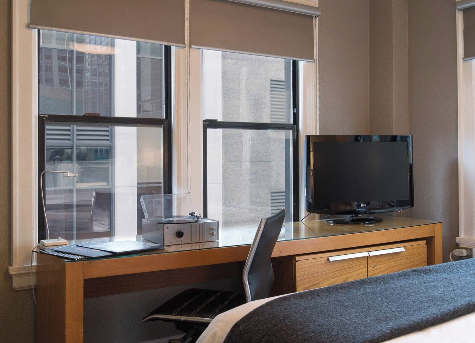 A hotel room with a desk, chair, TV, and a bed.