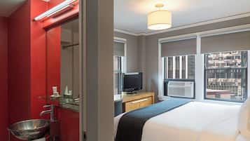 A hotel room with a bed, a TV, an air conditioning unit, a window with a view, and a red wall.