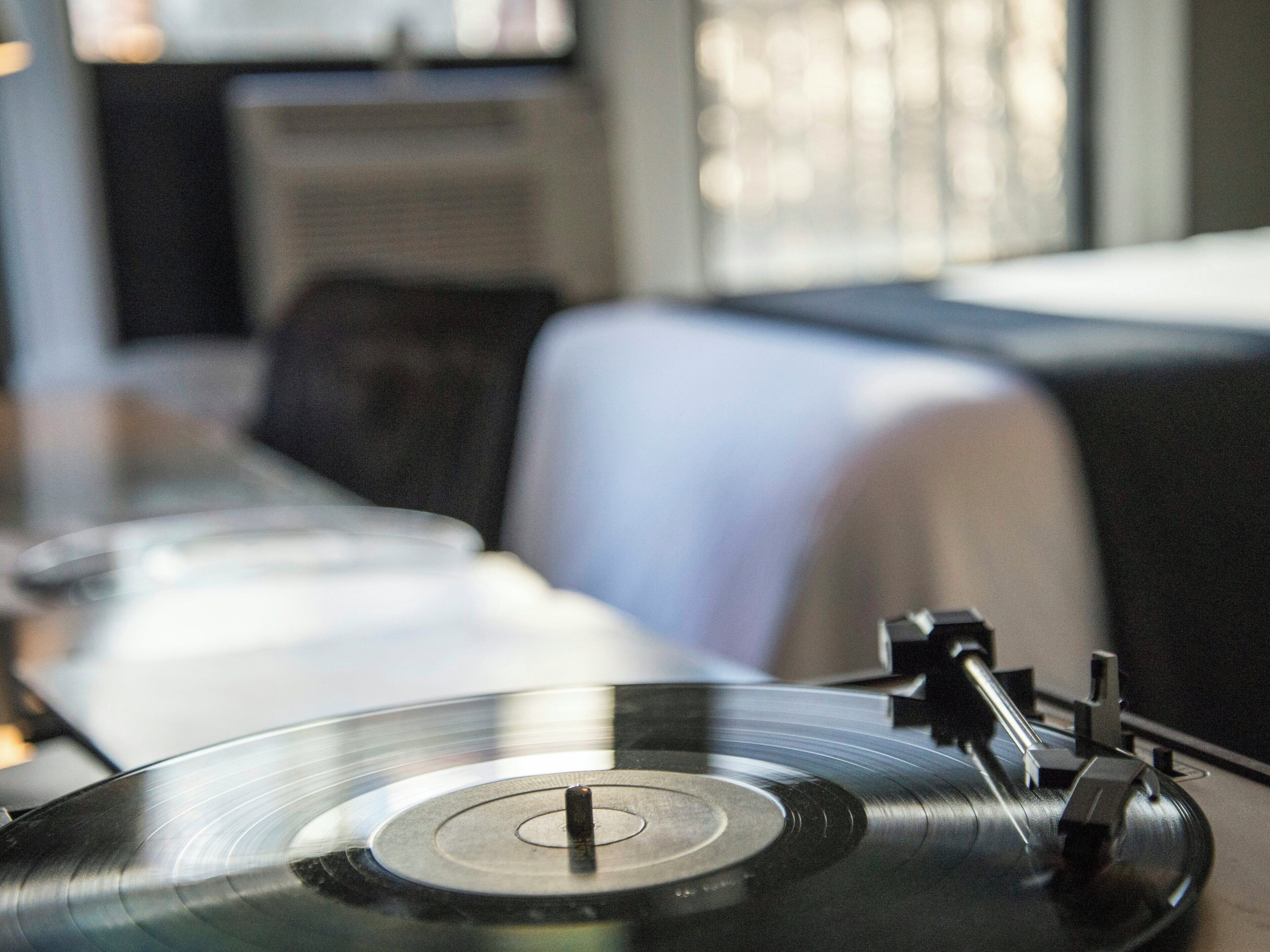 A turntable with vinyl records, a sofa, and a window in the background.