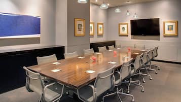 Una sala de conferencias con una mesa larga, sillas, obras de arte enmarcadas y un televisor de pantalla plana.