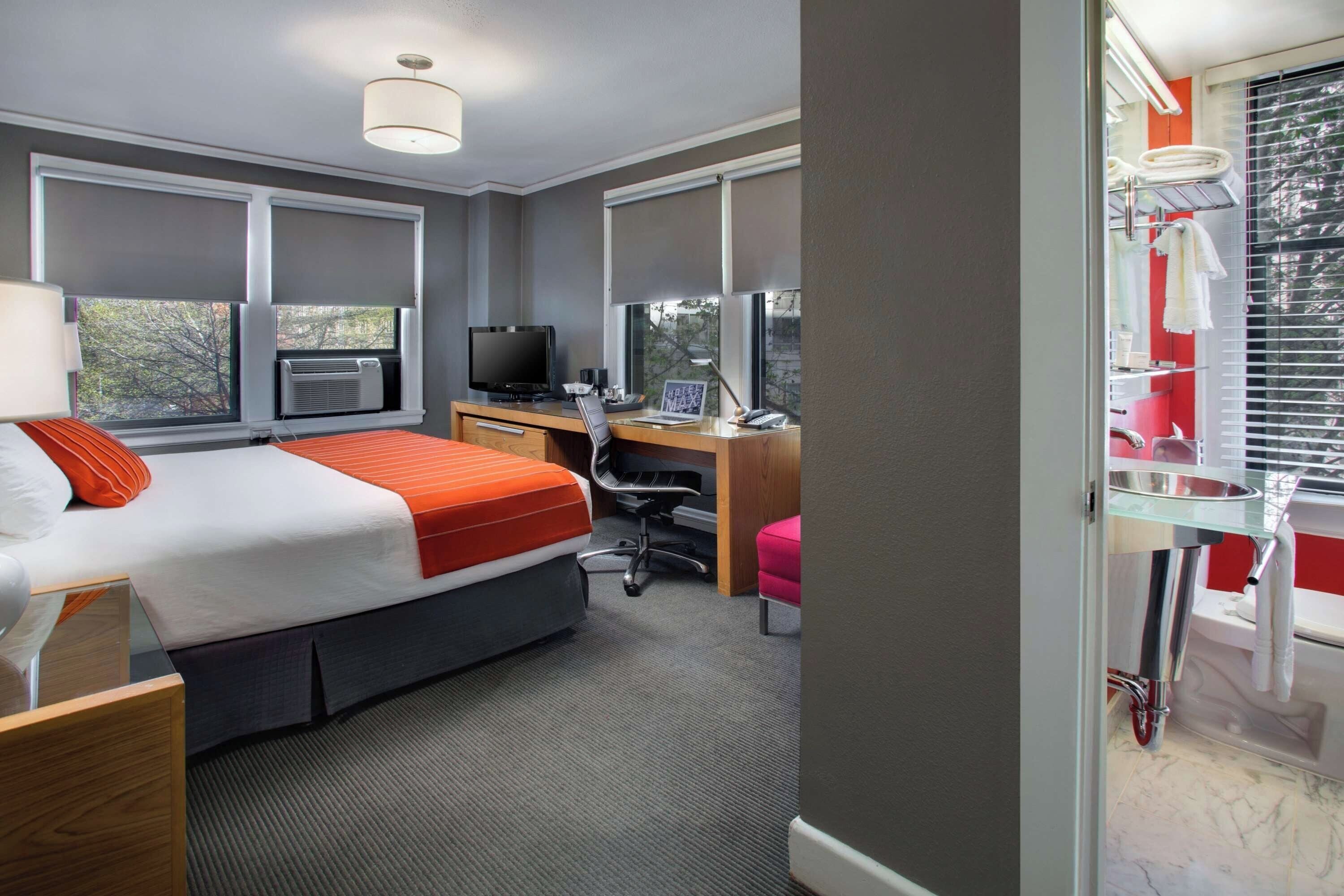 Een hotelkamer met een bed, bureau, stoel, en een badkamer met een wastafel en douche.