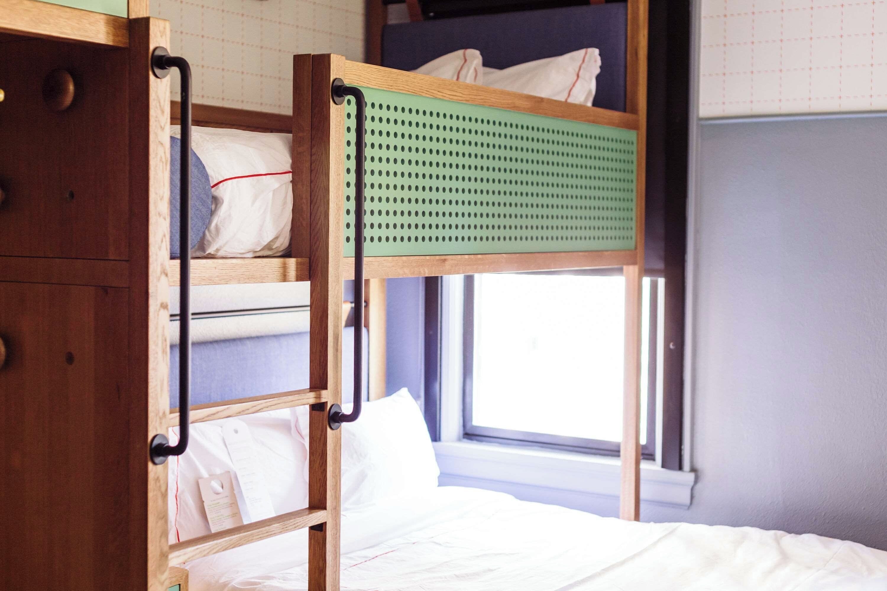 A bunk bed with a wooden frame, a green headboard, and white bedding.
