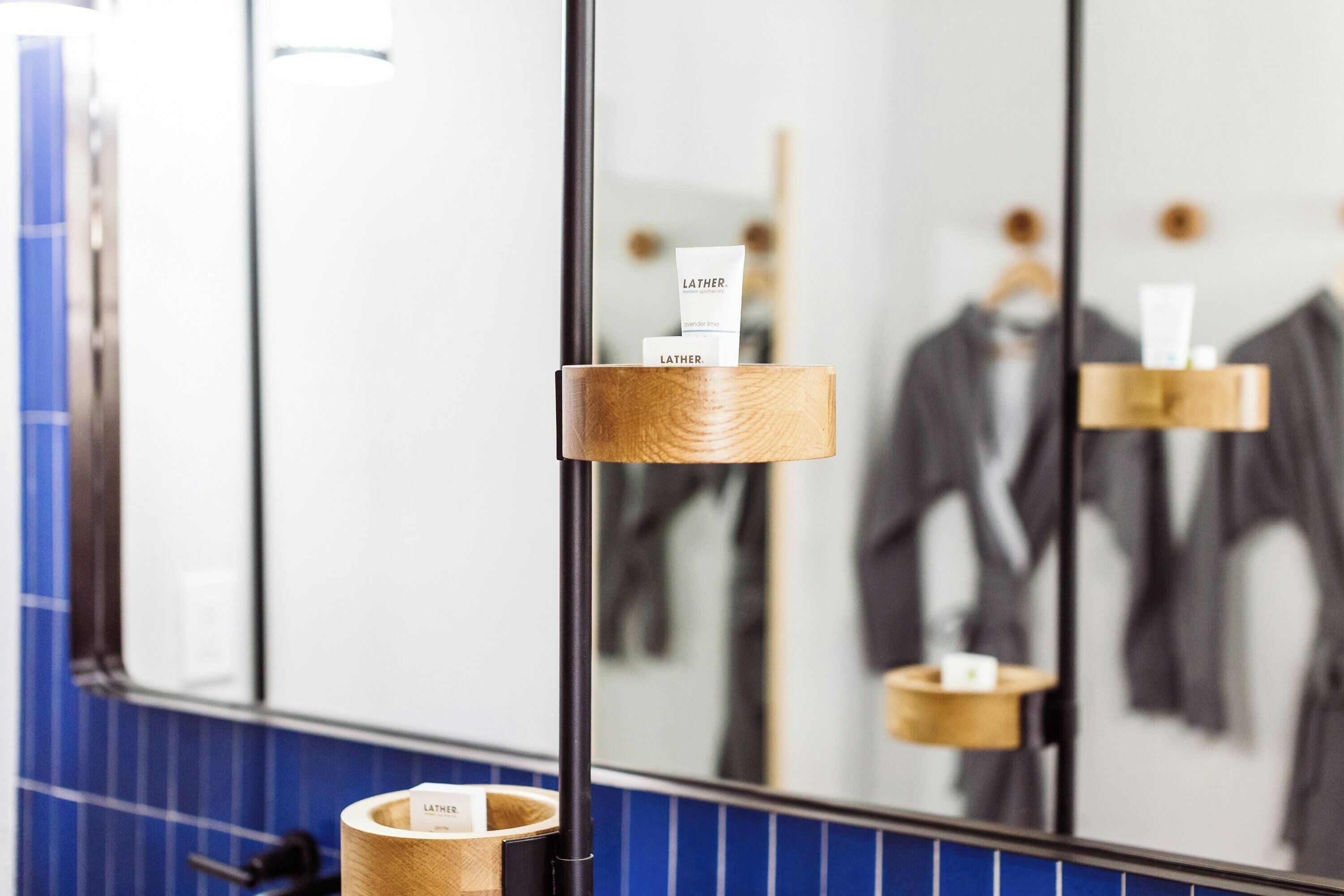 A bathroom with a mirror reflecting a suit rack and a towel dispenser.
