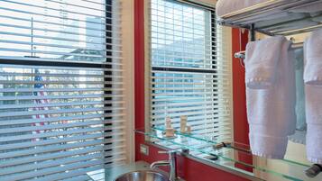 A modern bathroom with a glass sink, a stainless steel faucet, and a glass shelf with toiletries.