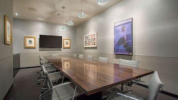 Une salle de conférence avec une longue table, des chaises, un téléviseur à écran plat, des tableaux encadrés et une grande peinture abstraite.