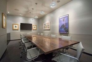 A conference room with a long table, chairs, a flat-screen TV, framed pictures, and a large abstract painting. - Hotel Max (Seattle)