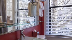 A bathroom with a glass shelf holding towels, a sink with a chrome faucet, and a window with blinds. - Hotel Max (Seattle)