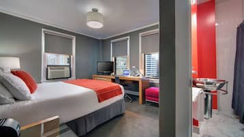 Habitación de hotel con cama, escritorio, televisión y baño con ducha y lavamanos.
